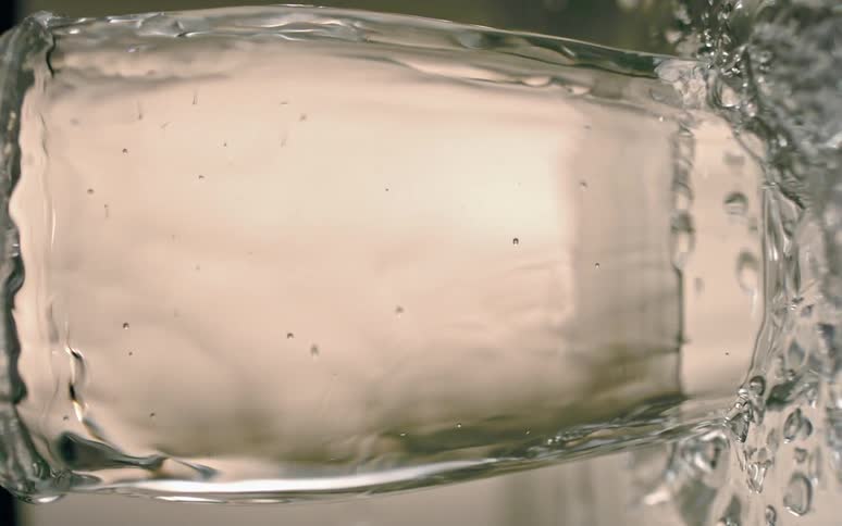 Crystal clear water overflows from a glass into a puddle
