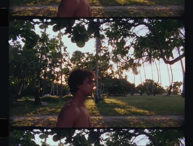 A shirtless surfer holding his board in an environment with lots of trees
