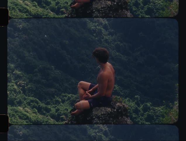 Man sitting on the peak of a mountain with tropical vegetation