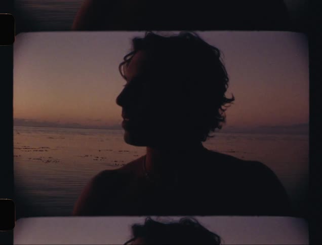 A shirtless man in an environment with water behind one morning