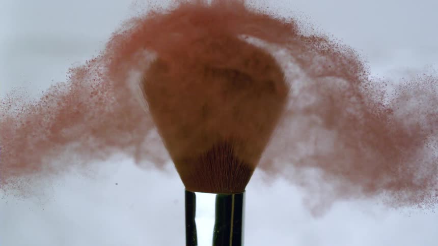 A fluffy make up brush twists as red powder flies everywhere