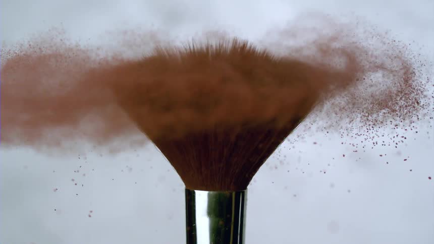 A makeup brush spinning and releasing brown powder