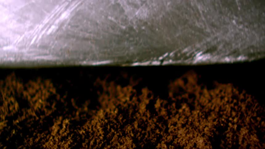 Light shines on coffee grounds as a silver object smashes down and they fly into the air