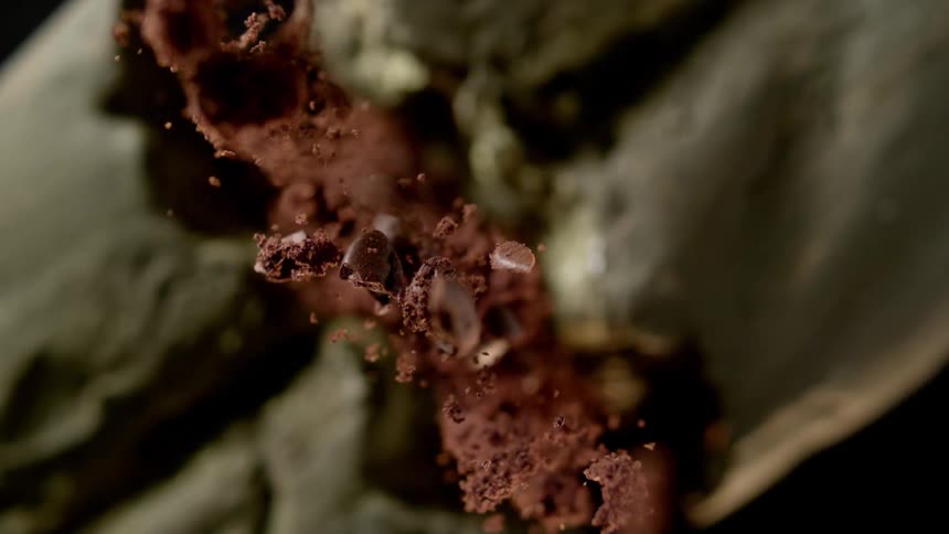Brown powder and particles fly into the air as an object breaks into two pieces