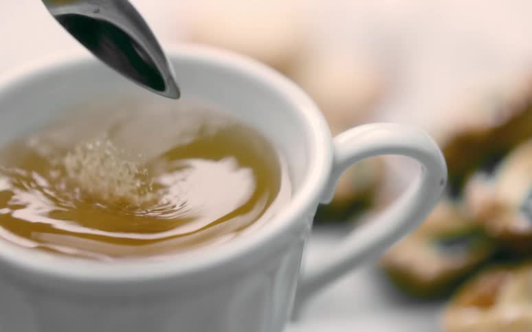 Spoon adds raw sugar into tea near pastries