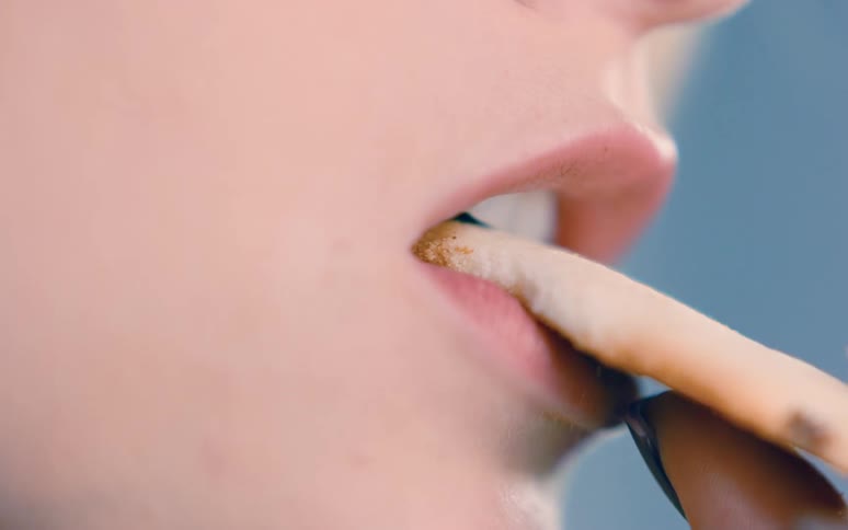 A girl holds a cookie in her mouth and bites off a piece