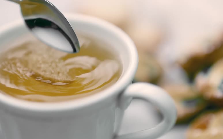 A spoonful of sugar drops into a teacup of yellow liquid