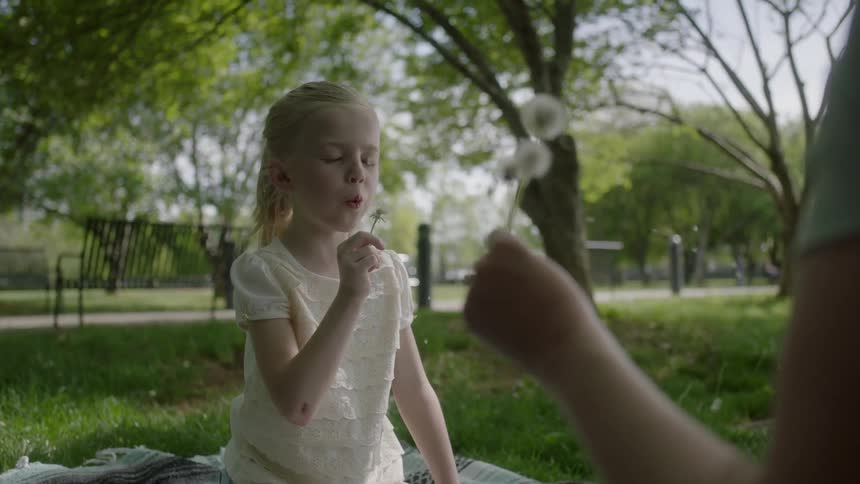 A woman hands a girl a flower to blow on