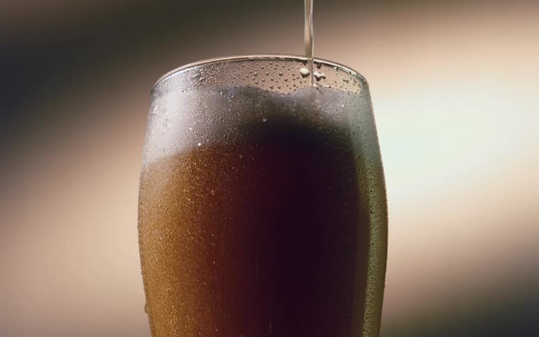 Beer is being poured into a glass already almost full of beer