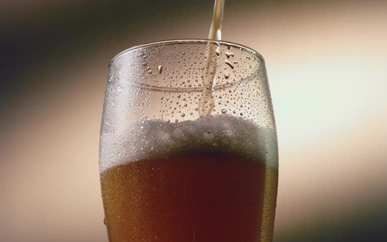 Water droplets cover a glass as cold beer pours in