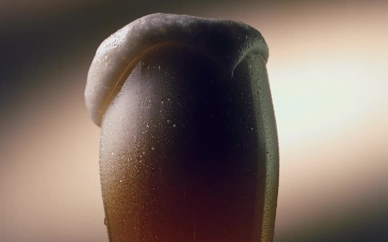The foam of a beer falling from the top of a glass