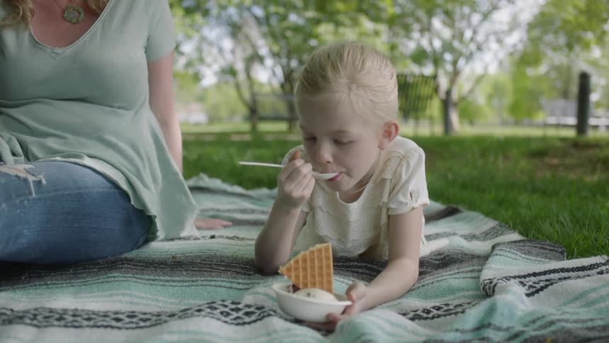 A child lays on a blanket in the grass eating ice cream