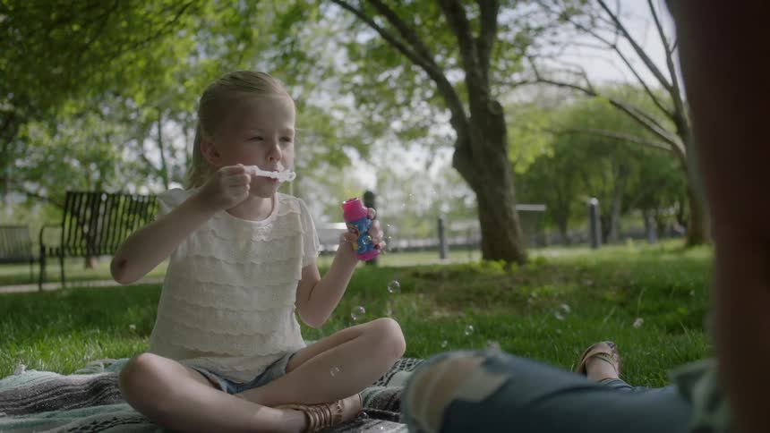 A girl is sitting on a blanket blowing bubbles