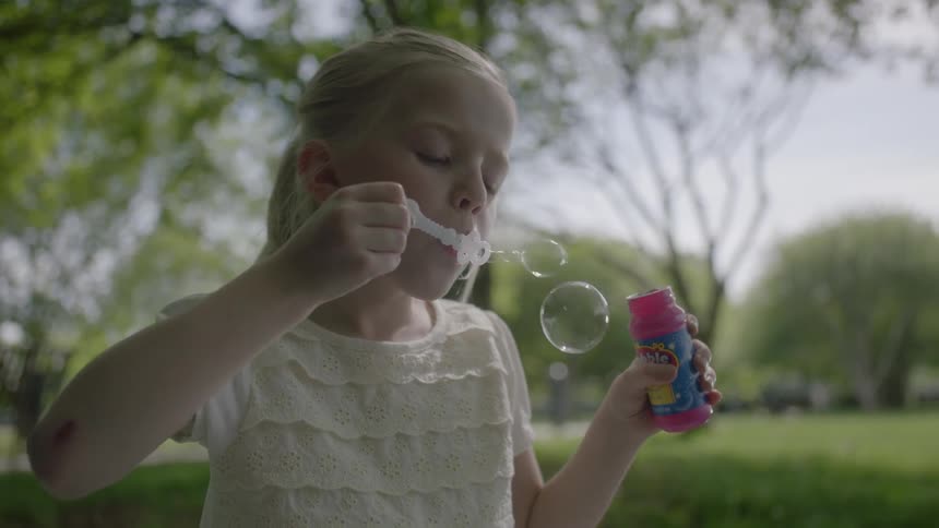 A girl is blowing bubbles on a green field