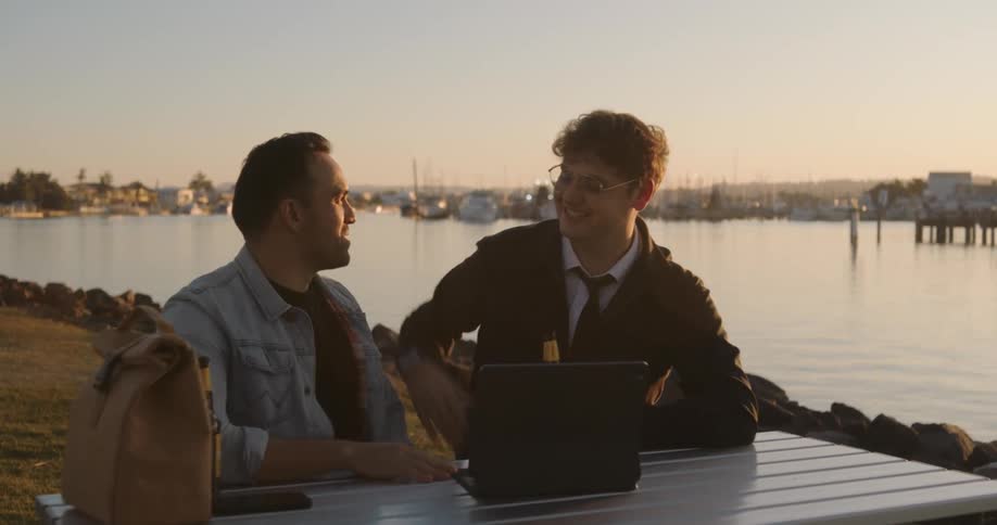 Friends sitting on shore at table celebrate after viewing results on laptop