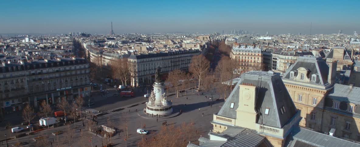 Traffic moves through area around plaza with a statue a long distance from the eiffel tower