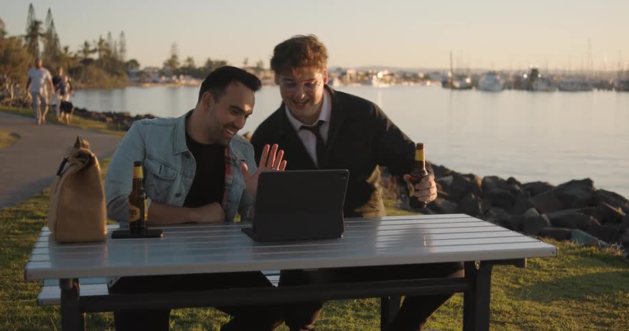 Two friends sitting near a lake have a video call