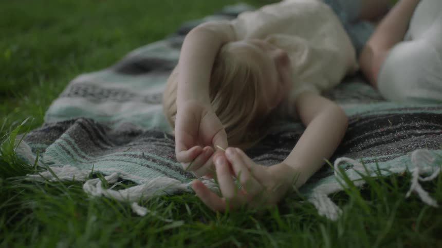 A girl plays with grass while laying on a blanket