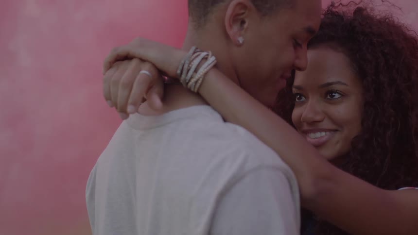 A woman puts her arms around a man with pink smoke all over