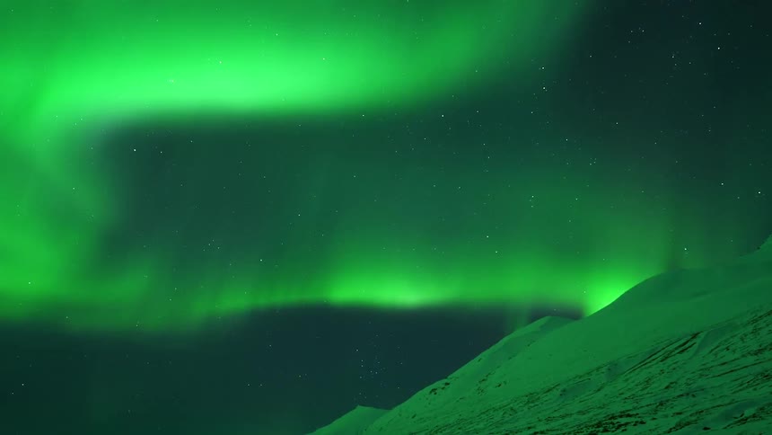 Green light of the aurora borealis fills the sky with mountain peaks in the foreground