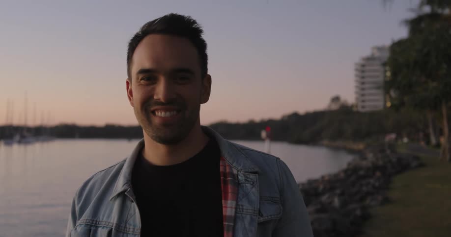 A man in a coat and beard smiling next to a lake