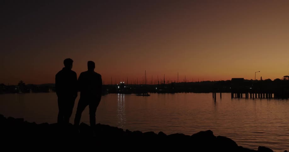 Silhouette of two friends by the river conversing under a reddish sky