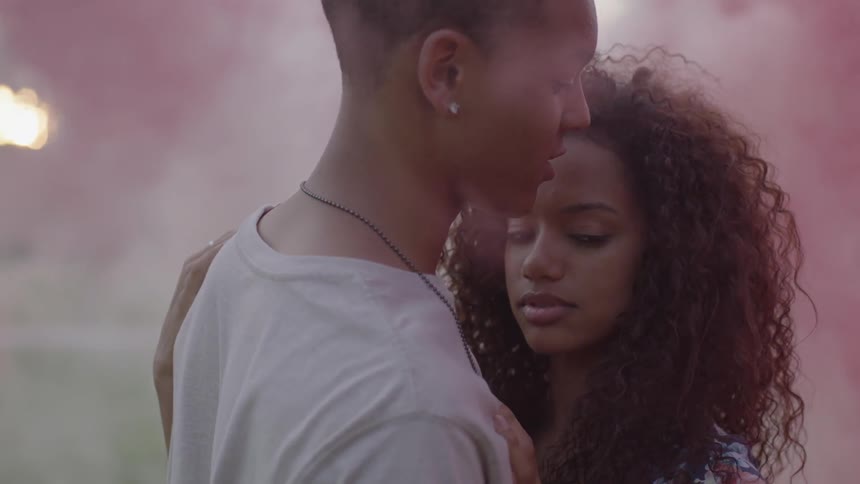 A man and woman are holding each other with pink smoke around