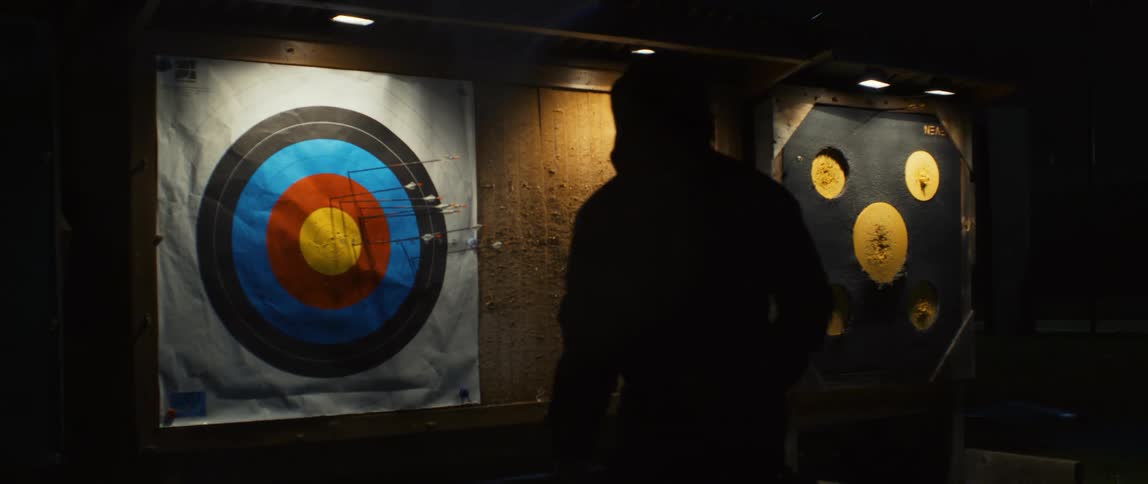 A silhouette of a person walking towards a target stuck in a wooden wall