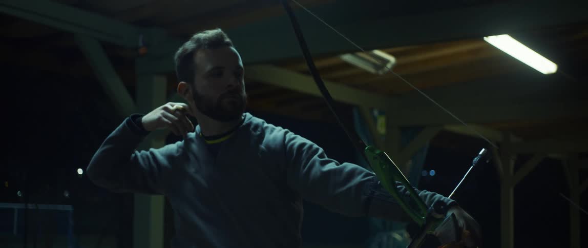 A bearded man shooting an arrow with a sports bow in a night