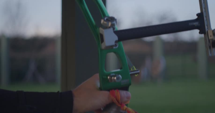 An adult shoots an arrow from a green compound bow in slow motion