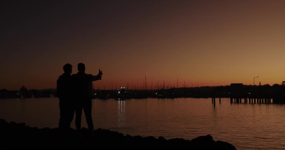 Two silhouettes of people next to a lake on an orange morning