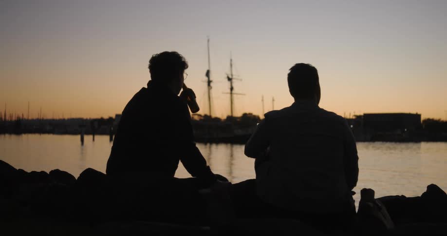 The silhouette of two men sitting drinking facing a lake