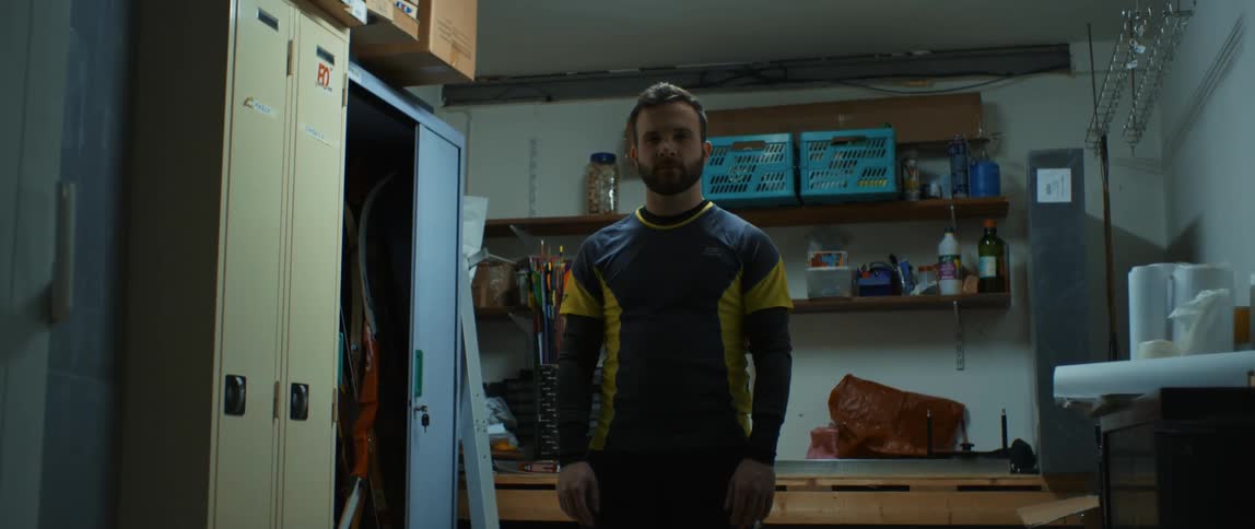 A man in athletic wear stands next to lockers in a room