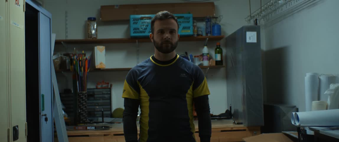 A bearded man stood inside a room staring straight ahead