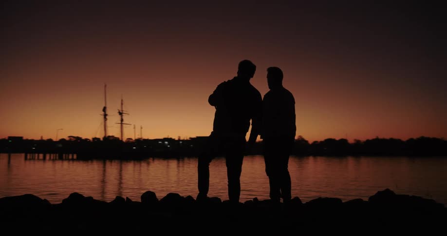 Two silhouetted men skip stones in a lake at sunset