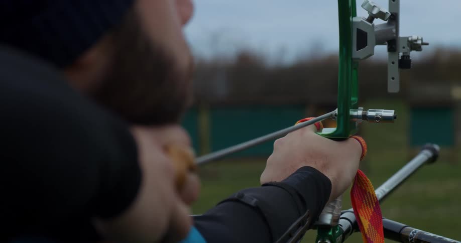 A man shoots an arrow with a compound bow across a sports field