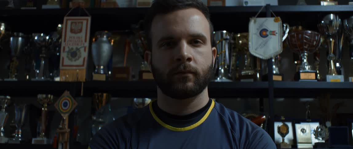 Portrait of a man with a serious expression and behind him a shelf with trophies