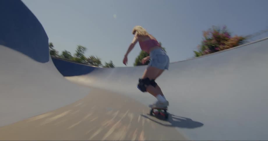 A young blonde woman is skateboarding at a concrete skatepark on a clear day