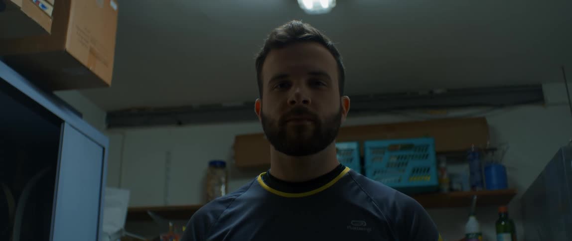 Bearded man standing in front of shelves gazing at the camera