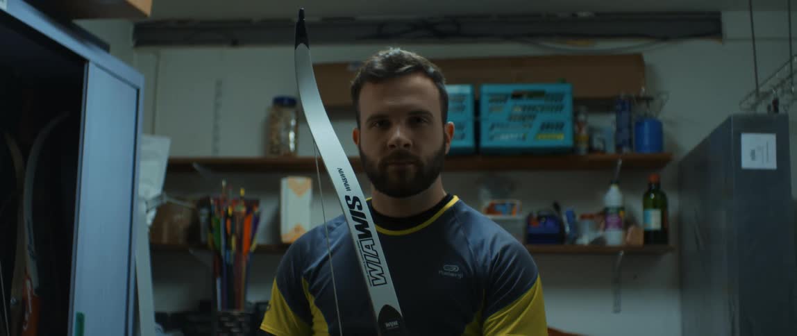 A man with a beard holding a bow inside a room