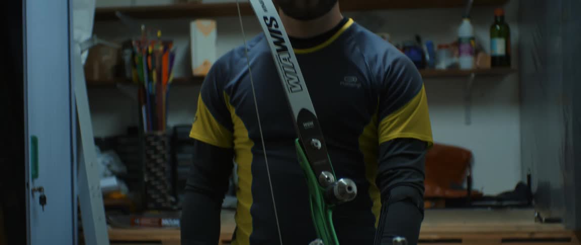 A bearded man in a coat holding a bow inside a room