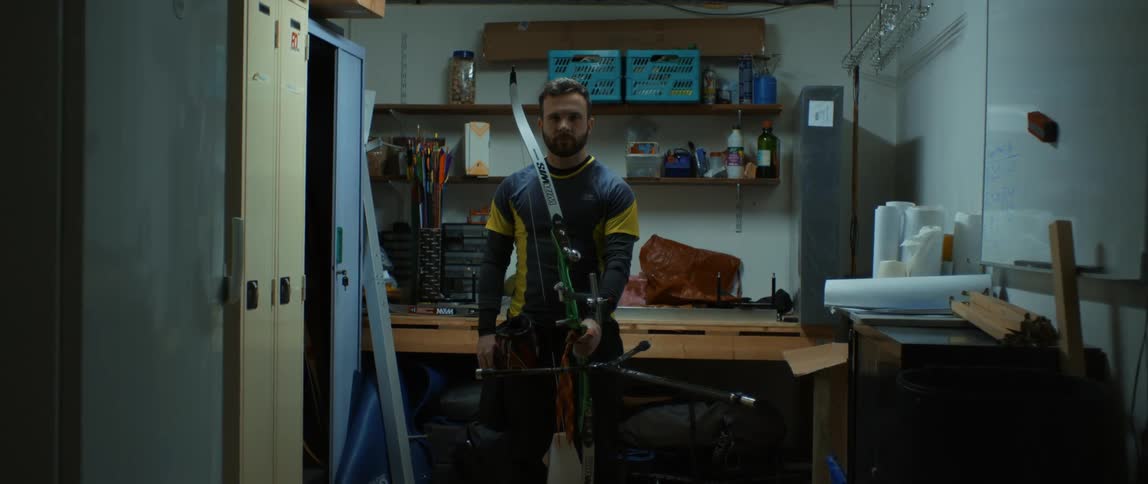A man stands with a bow and arrow in hand and stares forward