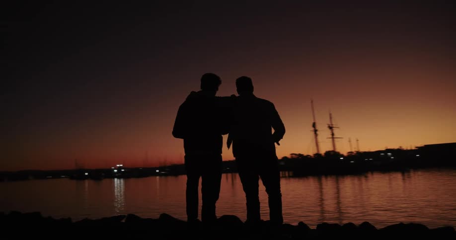 Two men hugging each other look at the lake on an orange morning