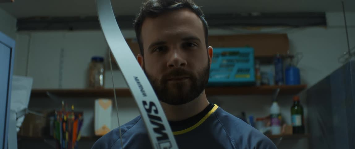 A man with a beard holding a bow and looking forward