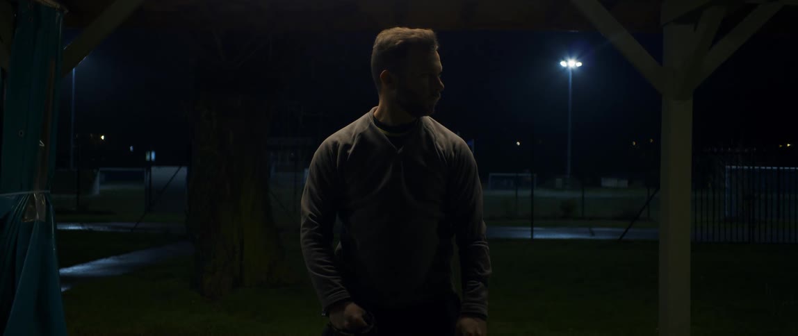 A man stand alone under a shade looking left and right at night