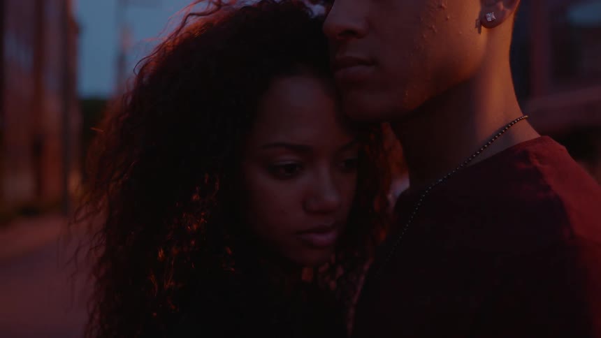 A man and woman hold each other in the street at dawn