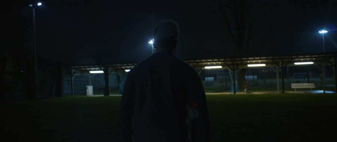 A man walking across a lawn to a penthouse with lights one night