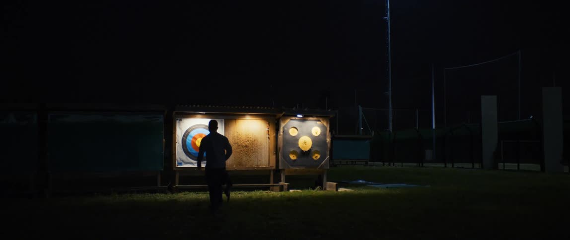 A man walks towards a circular target on an archery field at night