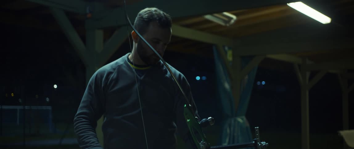 A bearded man in a coat nocking an arrow into a competition bow