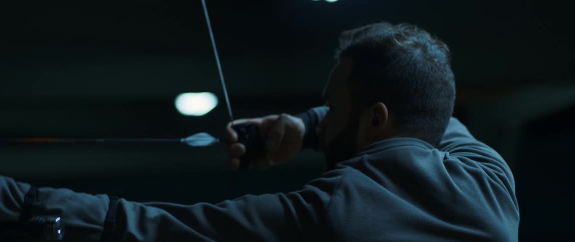 A bearded man points the bow and arrow towards the target